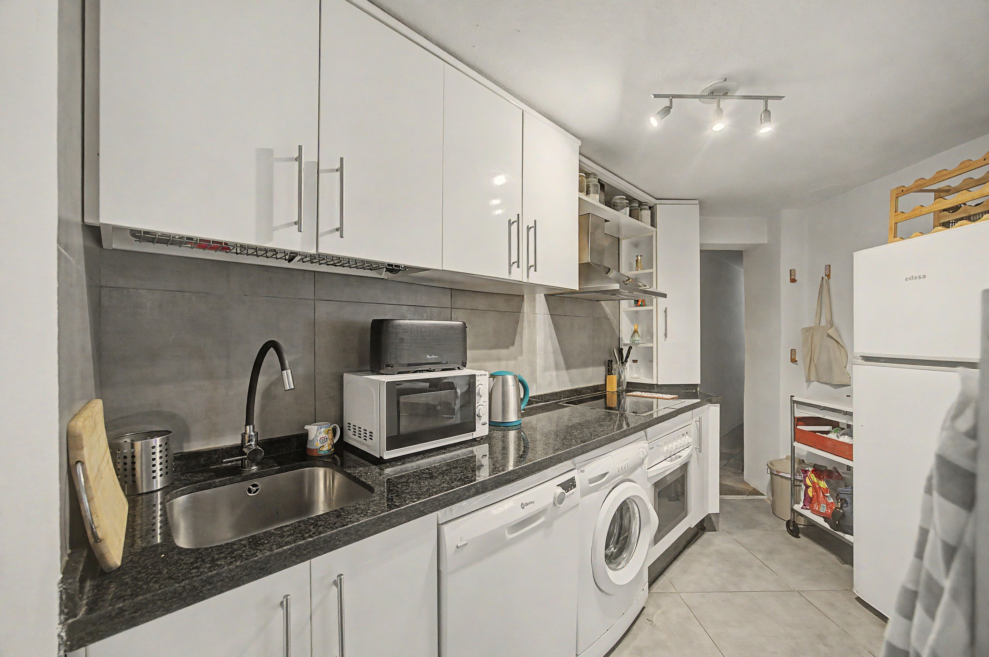 A modern kitchen with white cabinets, a built-in microwave, a sink, and a washing machine.