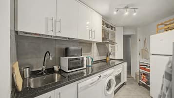 A modern kitchen with white cabinets, a built-in microwave, a sink, and a washing machine.