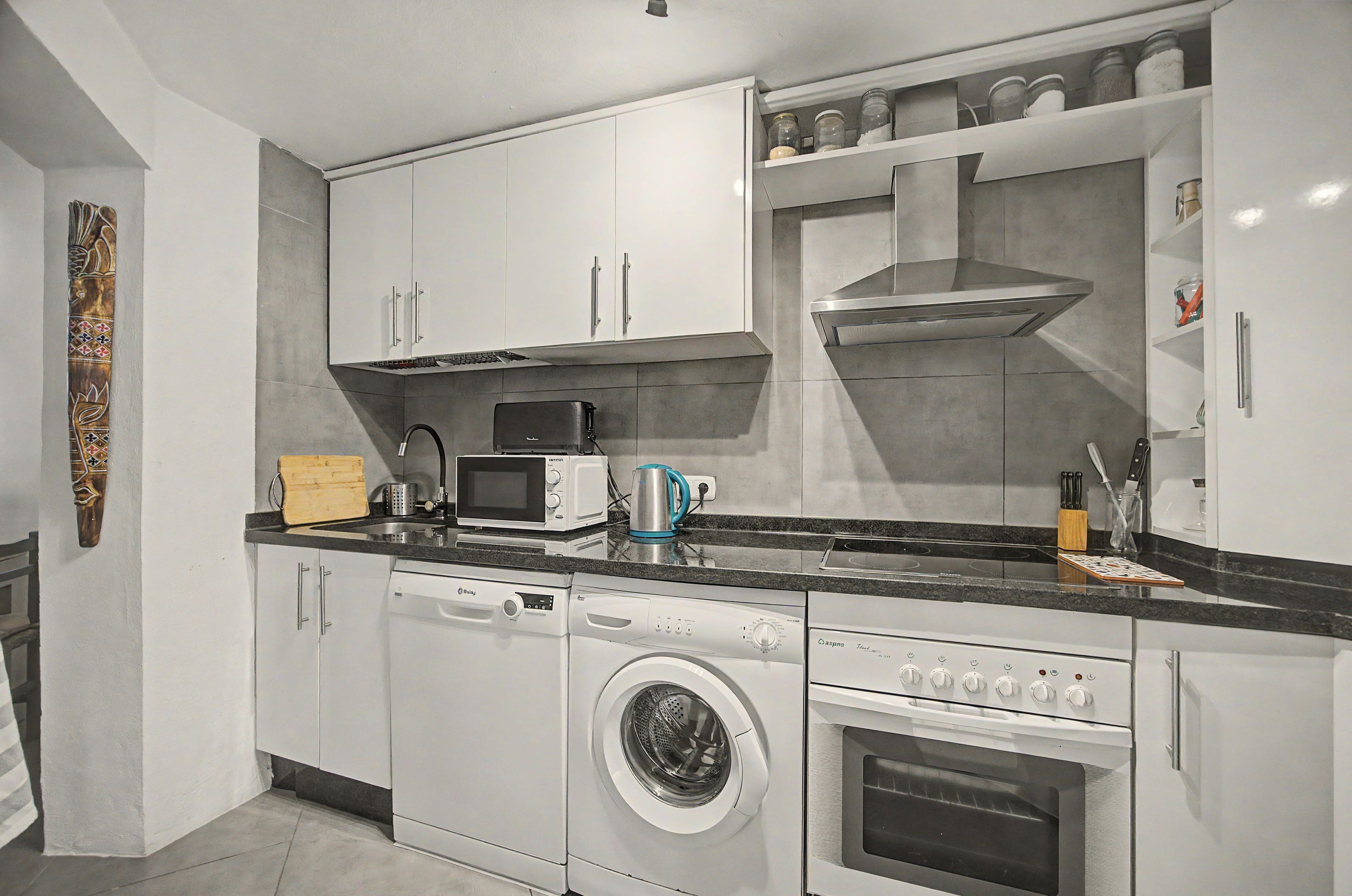 A modern kitchen with white cabinetry, a built-in microwave, a coffee maker, a dishwasher, and an oven.
