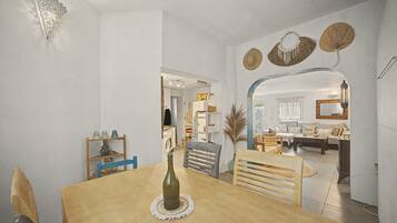 A dining area with a wooden table, chairs, and a bottle of wine. There is a kitchen in the background with a washing machine and cabinets.