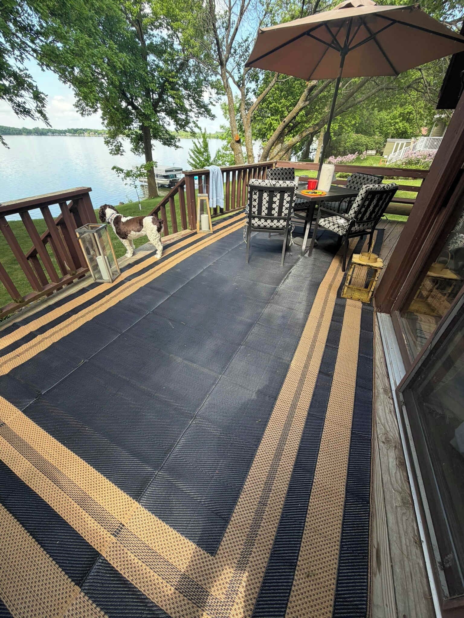 Eine Terrasse mit schwarzem und gelbem Streifenmuster, Gartenmöbeln und Blick auf einen See.
