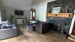 Ein Wohnzimmer mit Kamin aus Stein, einem an der Wand befestigten Fernseher und einem grauen Ecksofa.