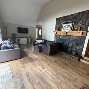 A living room with a stone fireplace, a television mounted on the wall, and a grey sectional sofa. - New - Lake Ida Cabin (Lake Park)