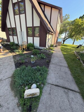 A modern house with a garden in front, a concrete pathway, and a body of water in the background. - New - Lake Ida Cabin (Lake Park)