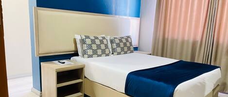 A hotel room with a bed, bedside tables, and a curtain.