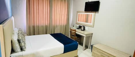 A hotel room with a bed, desk, chair, and a television on the wall.