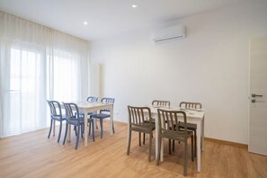 A dining area with two tables, each with six chairs. There is a window with curtains, an air conditioning unit on the wall, and a door to the right. - New Room 4 near Venice | Private Bathroom and AC (Malcontenta)