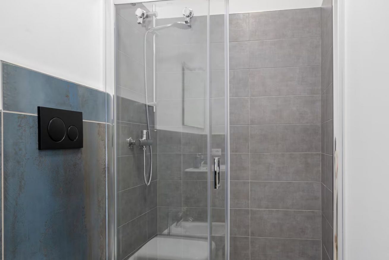 Una ducha con puerta de cristal, un cabezal de ducha manual y un grifo empotrado en la pared.