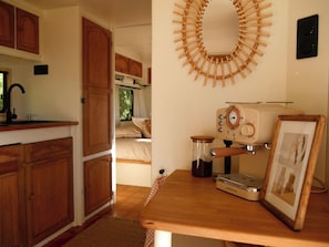 A compact kitchen with wooden cabinets, a coffee machine, and a wall-mounted circular bamboo decoration.