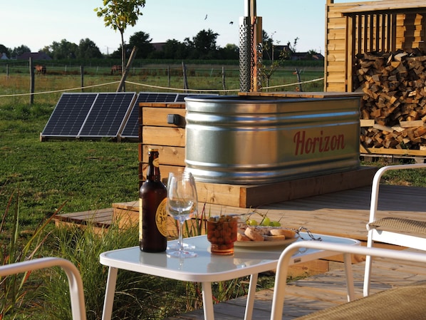 A wooden deck with a metal barrel labeled 'Horizon,' a bottle, a glass, and a plate with food.