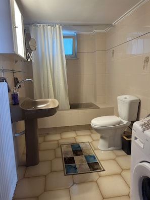 A bathroom with a sink, toilet, bathtub, and a washing machine. - Kastelia Monemvasia (Monemvasias)