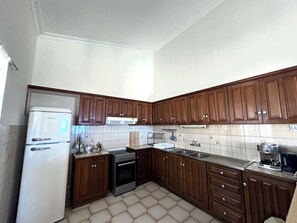 A kitchen with wooden cabinets, a white refrigerator, a stove, and a sink. - Kastelia Monemvasia (Monemvasias)