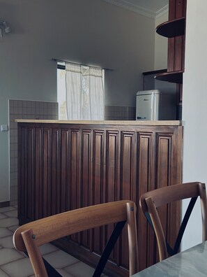 A kitchen with a wooden cabinet, a refrigerator, and a window with curtains. - Kastelia Monemvasia (Monemvasias)