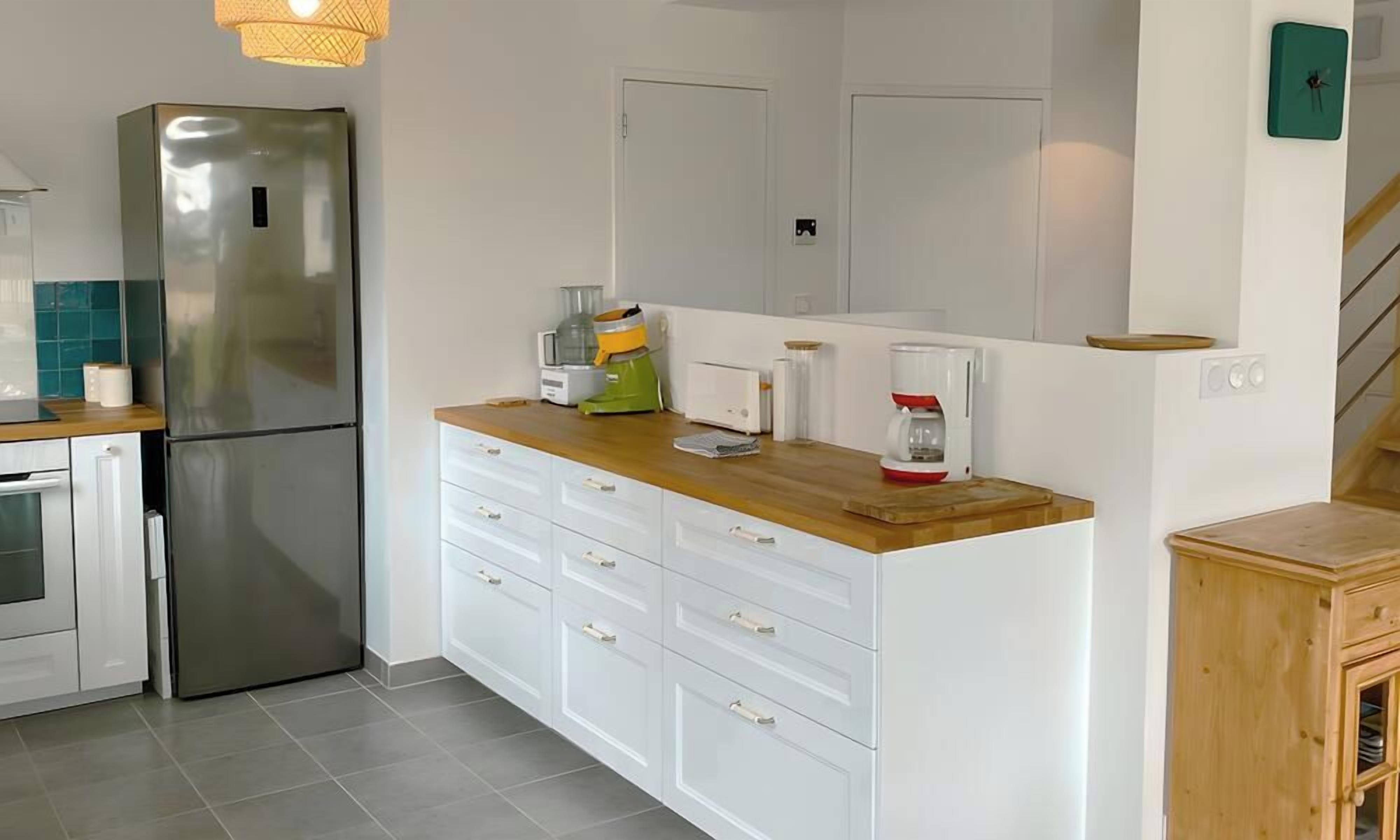 Una cocina moderna con refrigerador de acero inoxidable, armarios blancos, encimera de madera y cafetera.