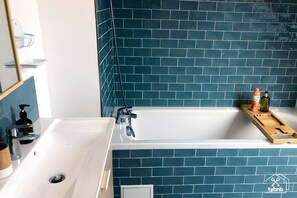 Une salle de bain avec une baignoire blanche, un miroir et un mur recouvert de carreaux bleus.