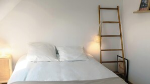 Un llit amb roba de llit blanca, una làmpada de nit i una escala de fusta adossada a la paret.