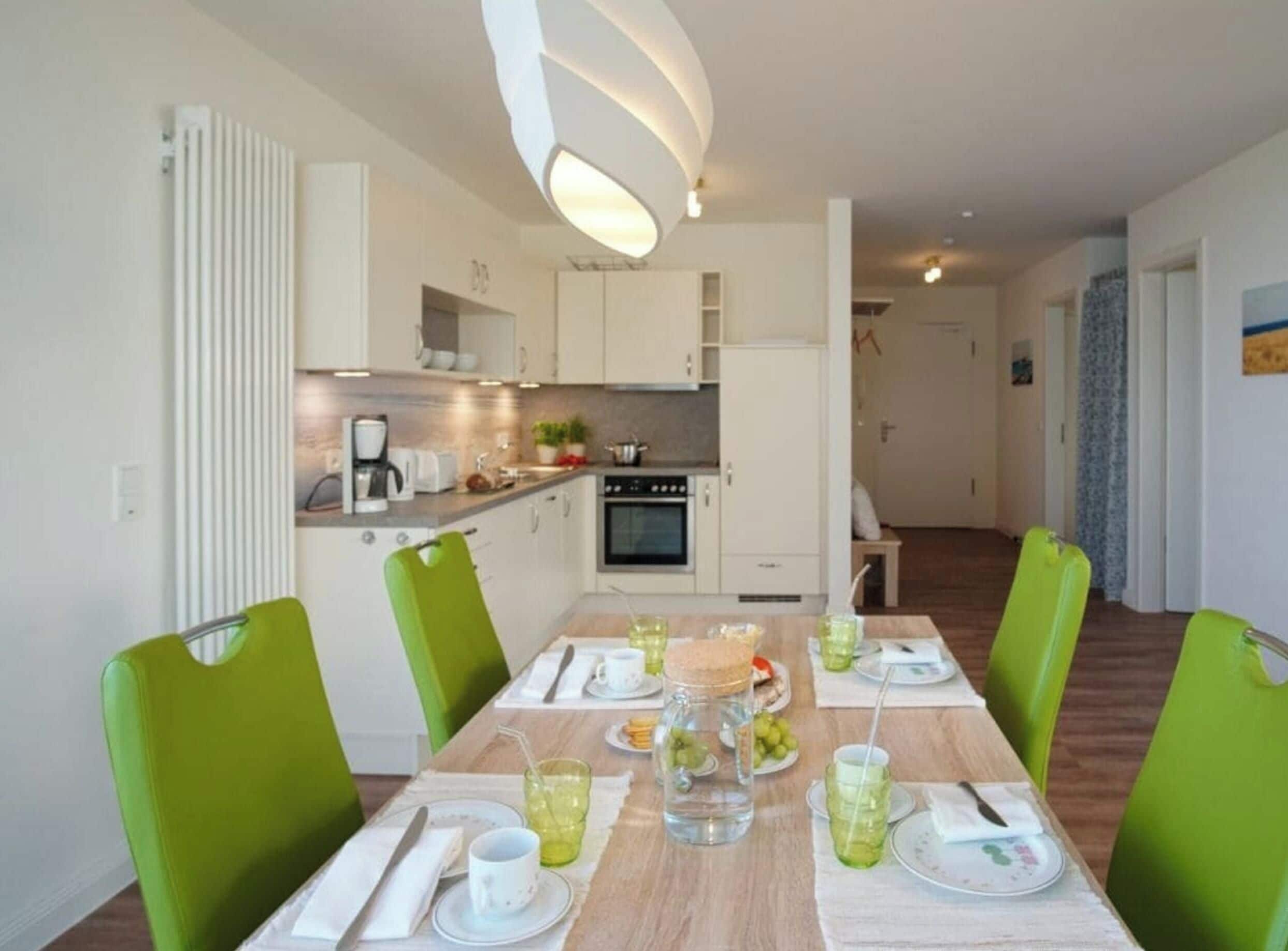 A modern kitchen with white cabinets, a built-in oven, and a dining area with a wooden table set for four.