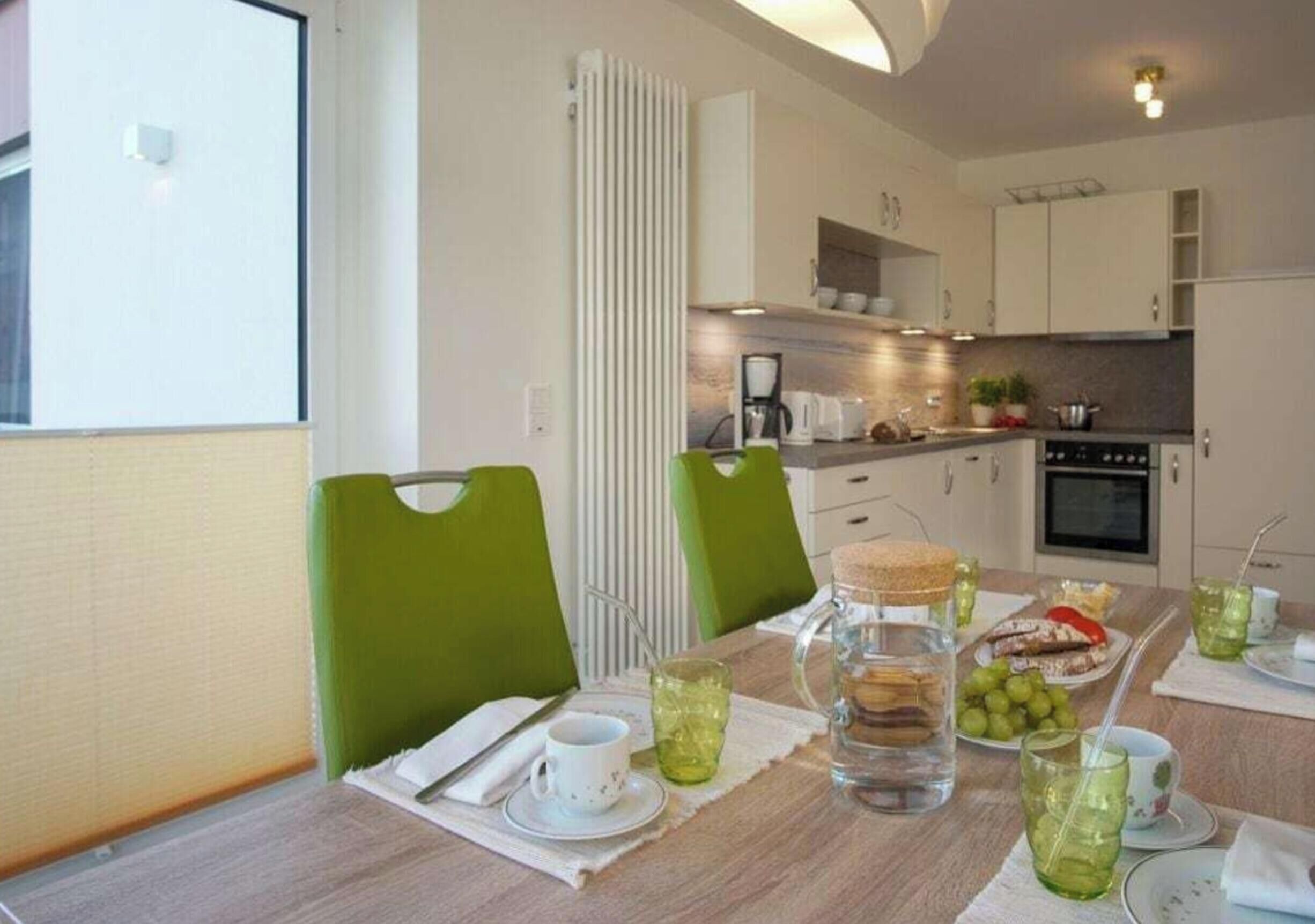 Een eethoek met een gedekte tafel voor twee personen, een koffiezetapparaat en een uitzicht op de keuken op de achtergrond.