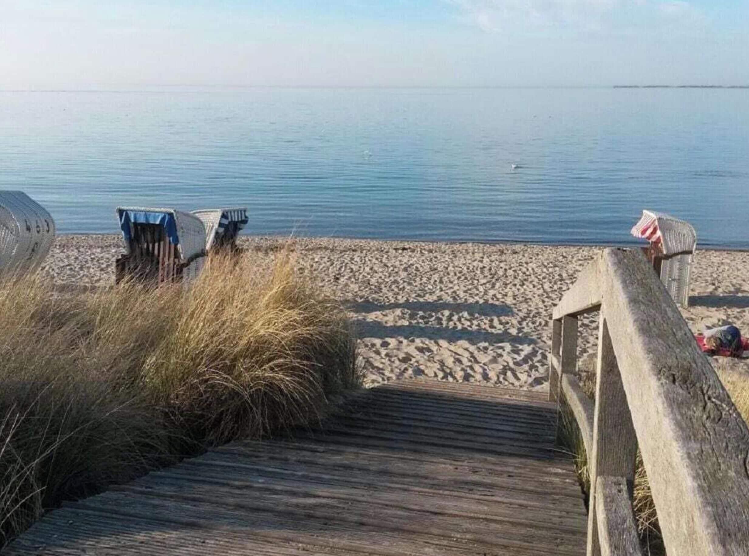A wooden boardwalk leading to a sandy beach with beach chairs and a small structure.