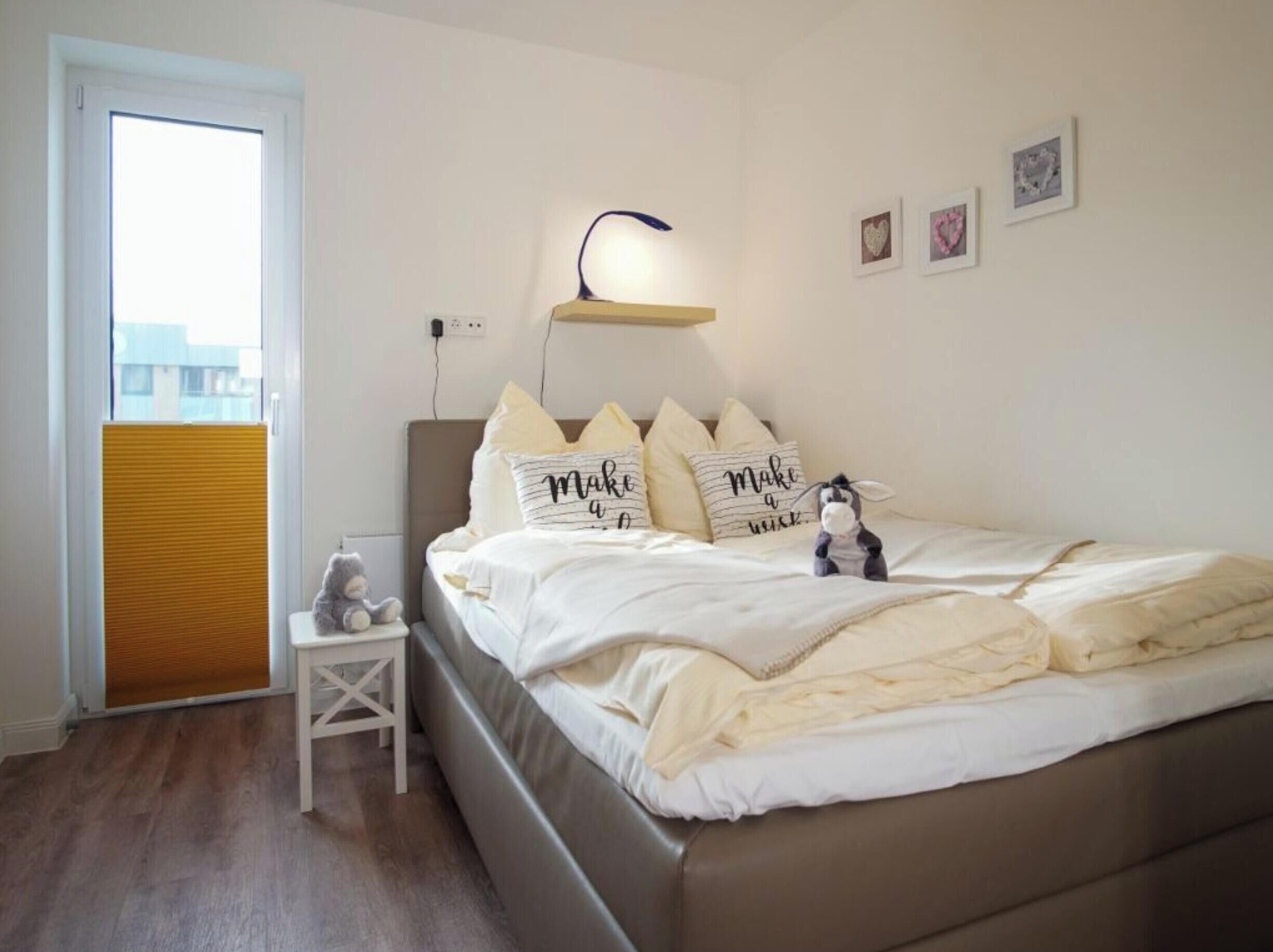 Quarto com cama, mesa de cabeceira, abajur e janela com persianas.