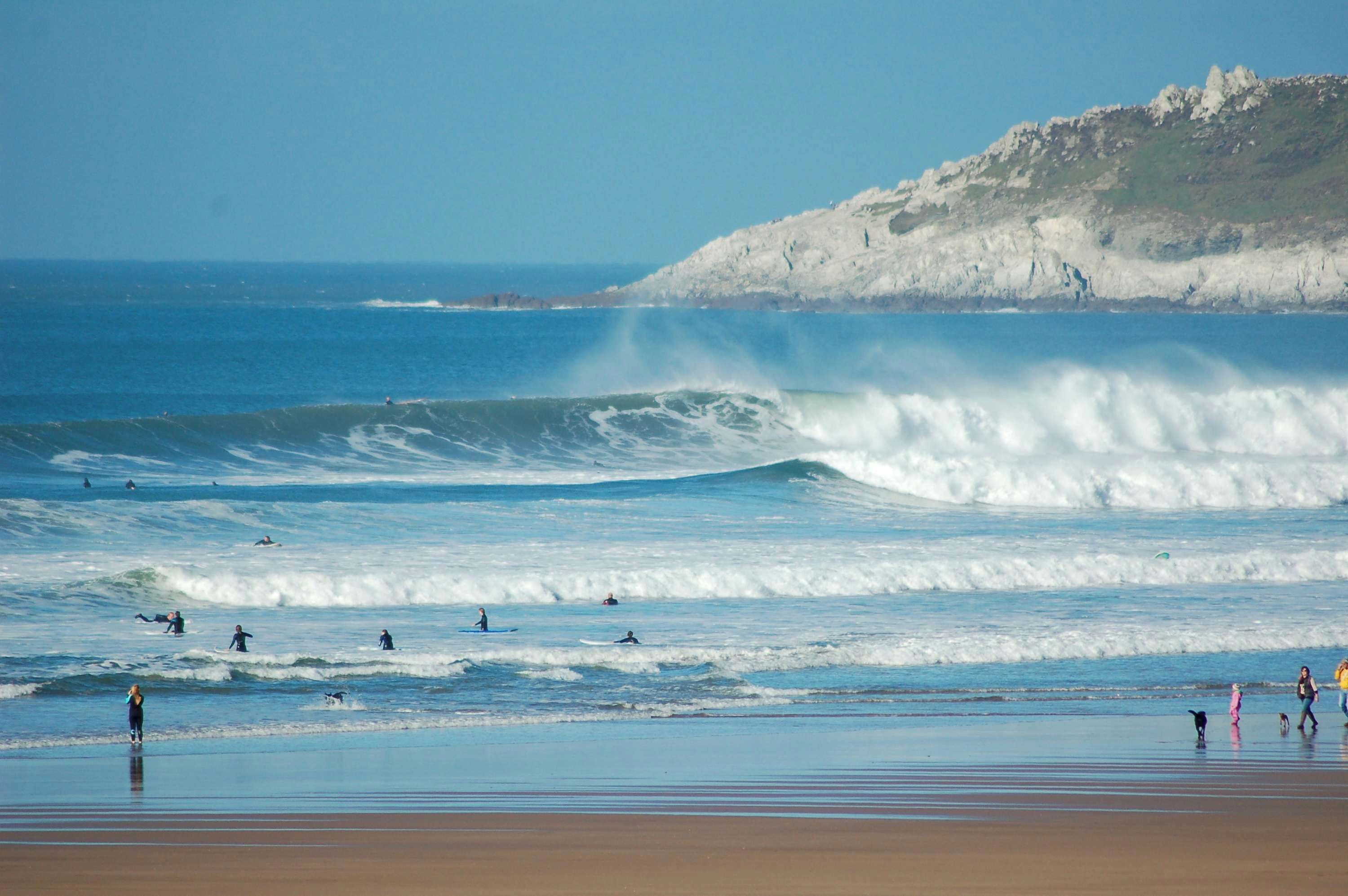 Une plage avec des vagues, une falaise et des gens dans l’eau.
