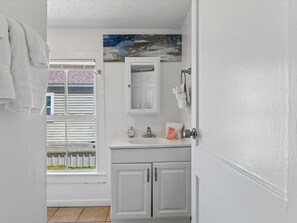 A bathroom with a white sink, a mirror, and a towel rack. - Beach Space Cottage | Steps to Beach! (Galveston)