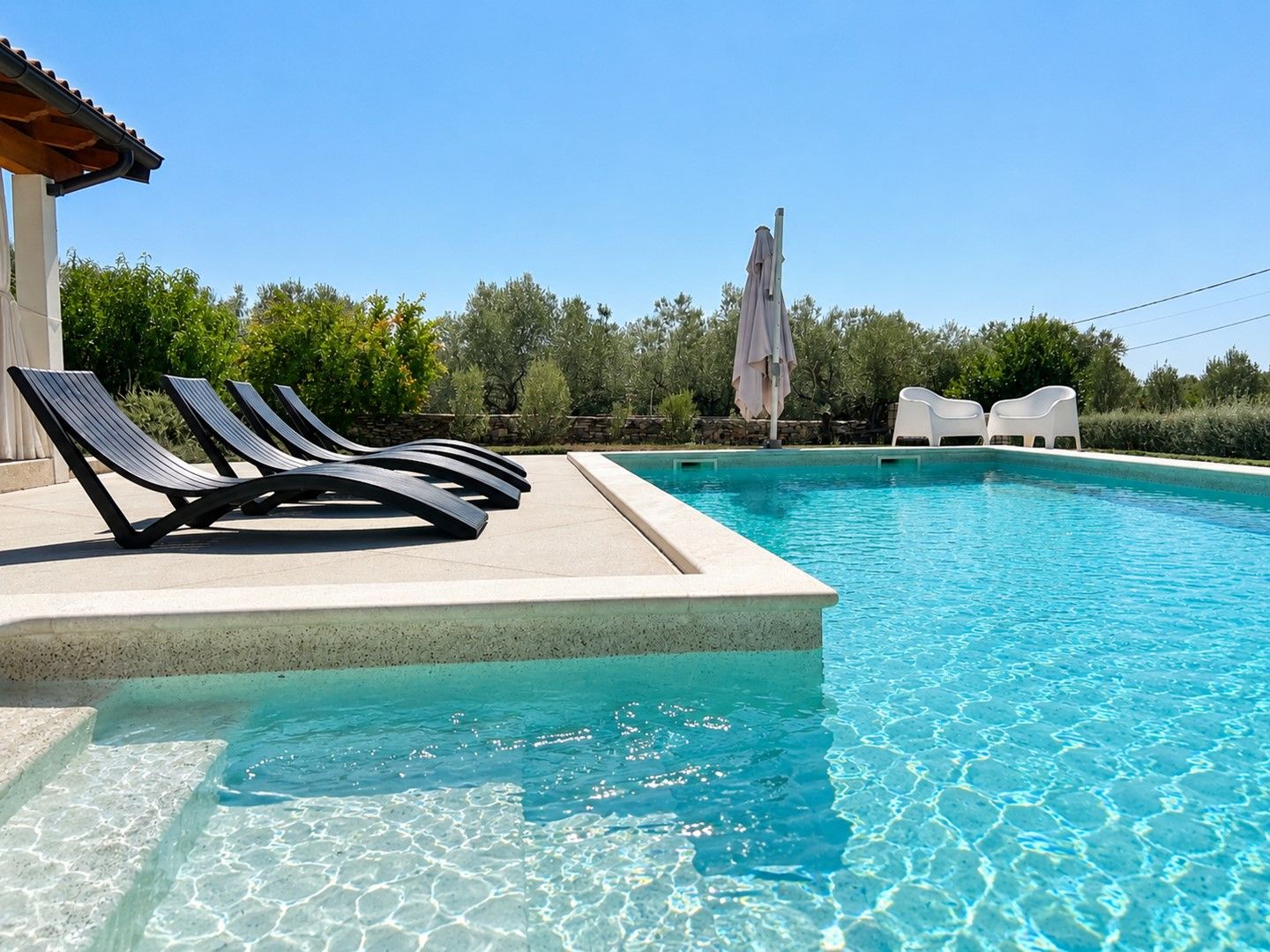 A swimming pool with lounge chairs and a stone wall.