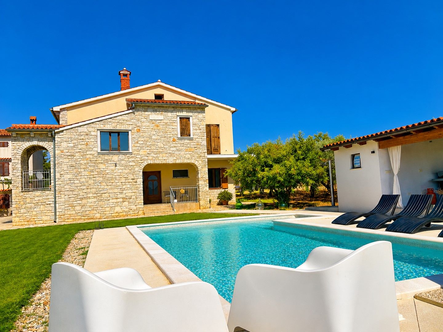 A two-story stone house with a swimming pool and lounge chairs.