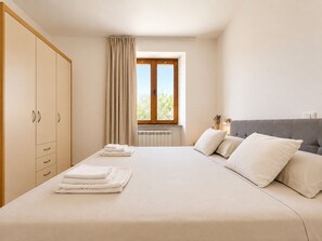 A bedroom with a bed, a wardrobe, a window with curtains, and a radiator. - Holiday House with Pool and Olive Trees (Galižana)