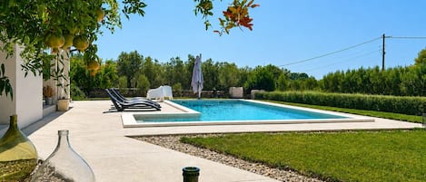A swimming pool with lounge chairs, surrounded by a well-maintained lawn and a hedge.