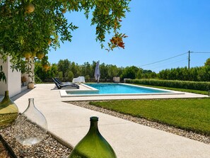 Una piscina con sillas de descanso, rodeada por un césped cuidado y un seto.