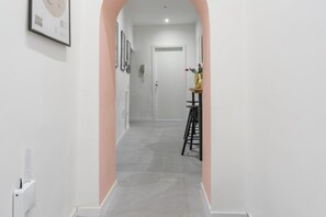 A hallway with a white door at the end, a small table with a vase of flowers, and a framed picture on the wall. - O' Buvero Suite Apartment By Dimorra  (Naples)