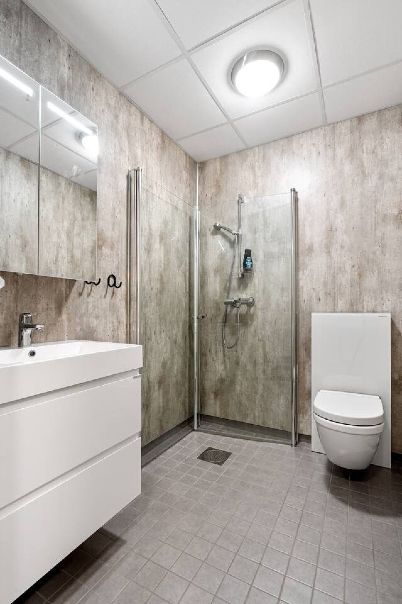 Ein modernes Badezimmer mit einer in Glas abgeschirmten Dusche, einem weißen Waschbecken und einer Toilette.