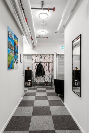 A hallway with a checkered floor, a coat rack with a jacket, and a large mirror on the wall. - Central Storgata Downtown Apartment (Tromsø)