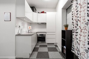 A compact kitchen with white cabinetry, a built-in oven, and a checkered floor. - Central Storgata Downtown Apartment (Tromsø)