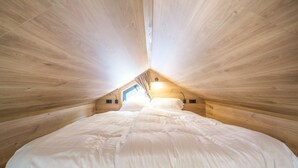 Ein Schlafzimmer mit Holzbalkendecke, einem Bett mit weißer Bettwäsche und einem Dachfenster.
