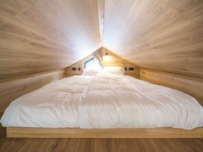 A bedroom with a wooden sloped ceiling, a bed with white bedding, and a skylight. - Resort Walsdorf - Tiny Loft with Hot Tub | 2p (Luxembourg)