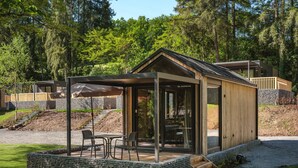 Eine Holzhütte mit Glastür und einer überdachten Terrasse mit Sitzgelegenheit.