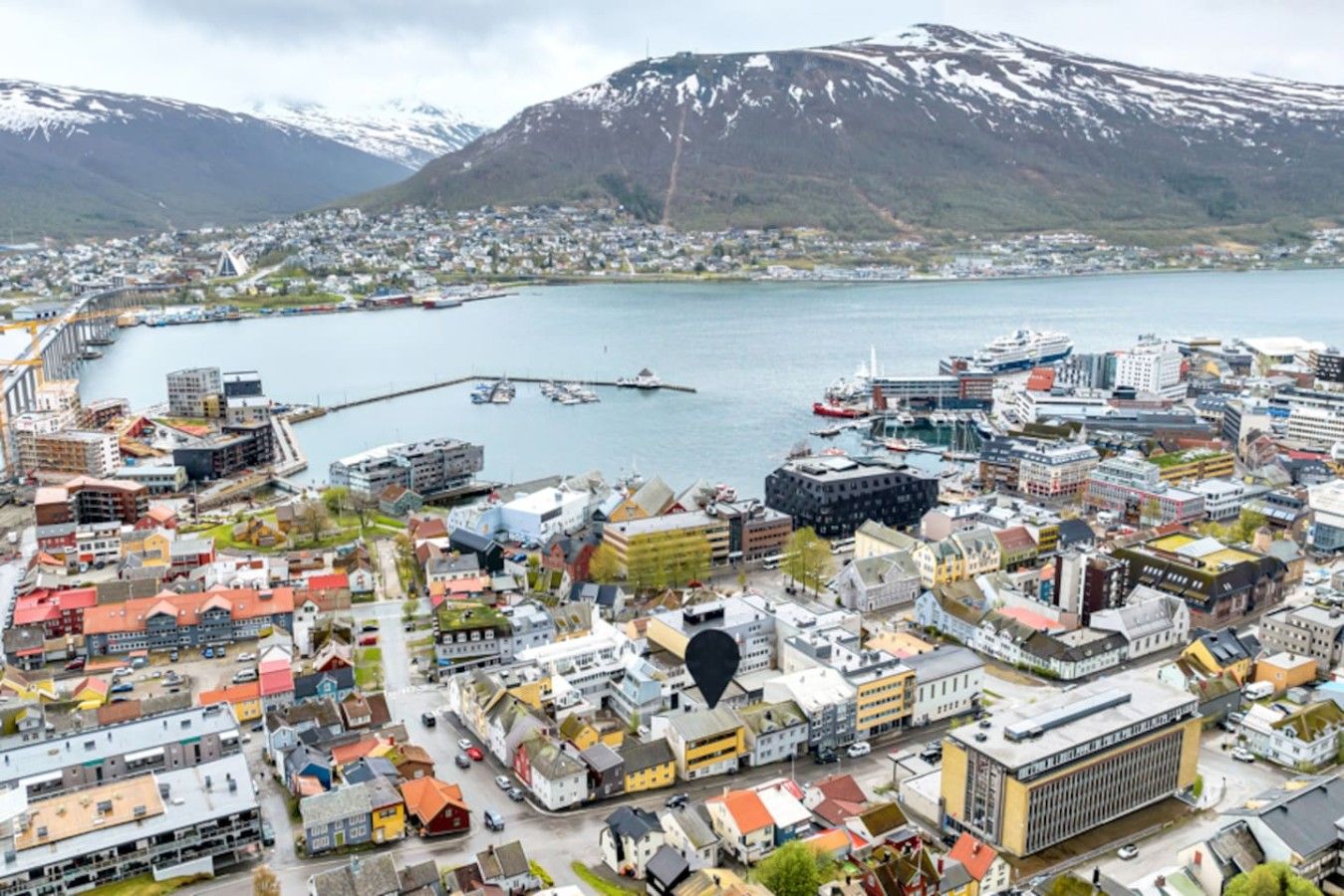 A coastal town with a marina, buildings, and mountains in the background.