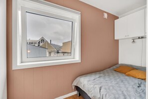 A bedroom with a bed, a window with a view of buildings, and a white wardrobe. - Modern Studio – Prime Central Location (Tromsø)