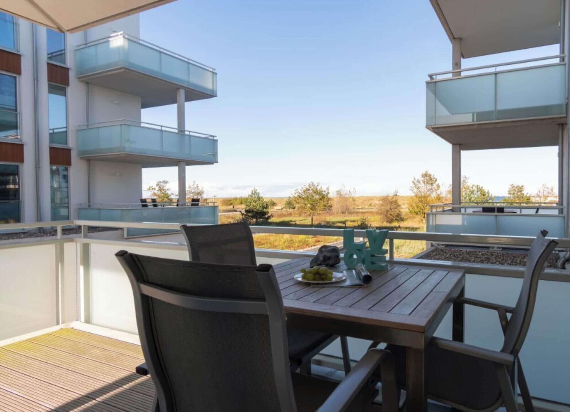 A balcony with a table and chairs, overlooking a landscape with trees and a clear sky.
