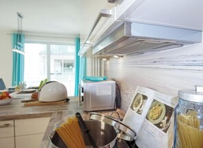 A modern kitchen with a microwave, a pot of spaghetti, and a cookbook on the counter. - Holiday Apartment With 2 Bedrooms (Heiligenhafen)