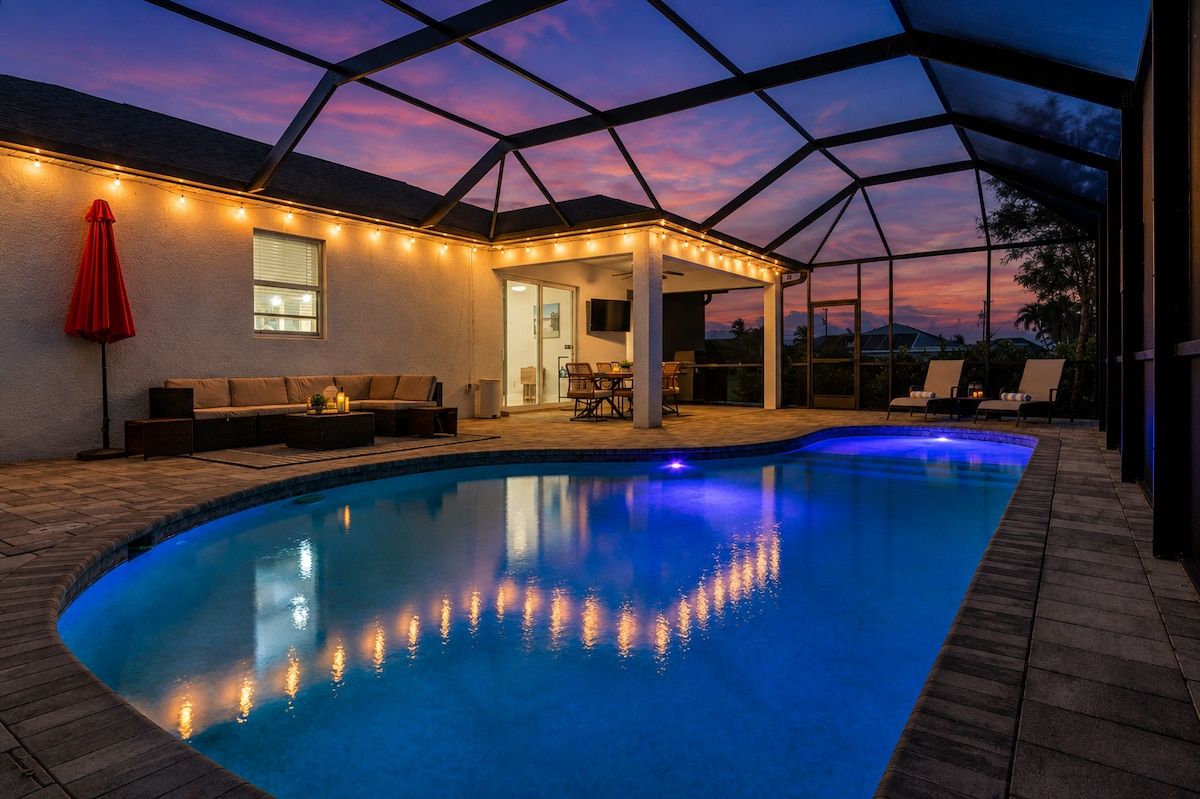 A swimming pool with a covered patio area, a red umbrella, and a sunset view.