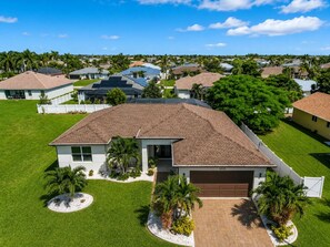 A single-story house with a garage, surrounded by a well-maintained lawn and palm trees. - Cape Coral home with Pool, Spa & Game Room (Cape Coral)