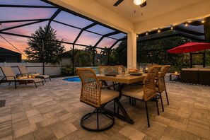 An outdoor patio with a dining table, chairs, and a pool. - Cape Coral home with Pool, Spa & Game Room (Cape Coral)