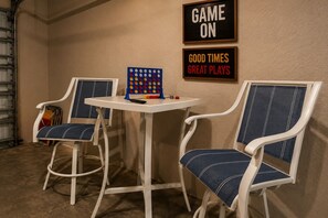 A room with two white chairs with blue cushions, a small table, and a board game. There are two framed signs on the wall, one reads 'GAME ON' and the other 'GOOD TIMES GREAT PLAYS'. - Cape Coral home with Pool, Spa & Game Room (Cape Coral)
