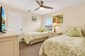 A bedroom with two beds, a ceiling fan, a TV, and artwork on the walls. - Cape Coral Home with Pool, Spa & Playful Beach House (Cape Coral)