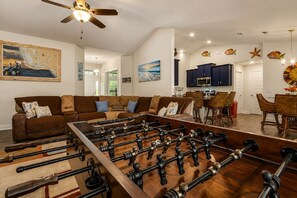 A living room with a foosball table, a brown sofa, and a ceiling fan. - Cape Coral Home with Pool, Spa & Playful Beach House (Cape Coral)