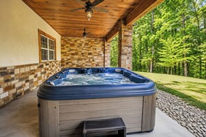 Un bain à remous installé à l’extérieur, avec un plafond en bois et un mur en pierre.