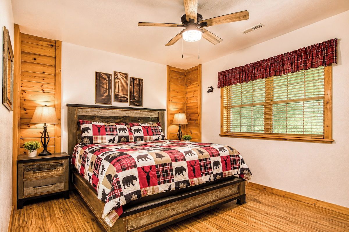 A bedroom with a bed, wooden walls, a ceiling fan, and a window with blinds.